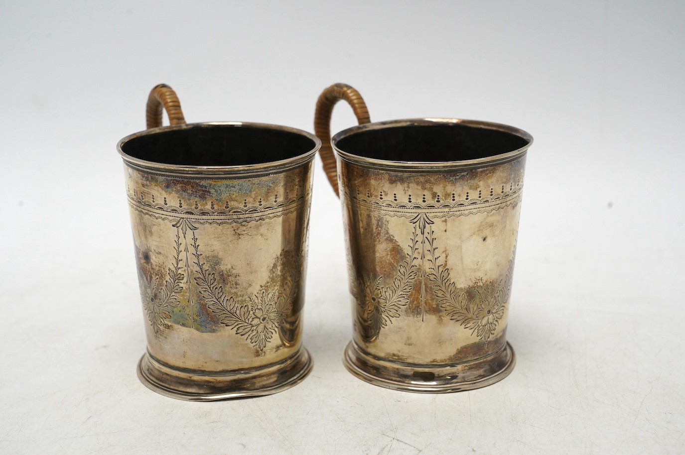 A pair of George V engraved silver mugs, with rattan handles, William Aitken, Birmingham, 1920, height 95mm, gross weight 5.9oz. Condition - fair